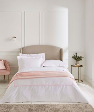 A white bedroom with a gray bed with white and pink bedding, a pink chair, and gray rug