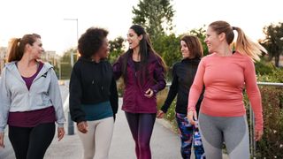 A group of women wearing active clothes working out together and laughing, walking along a bridge