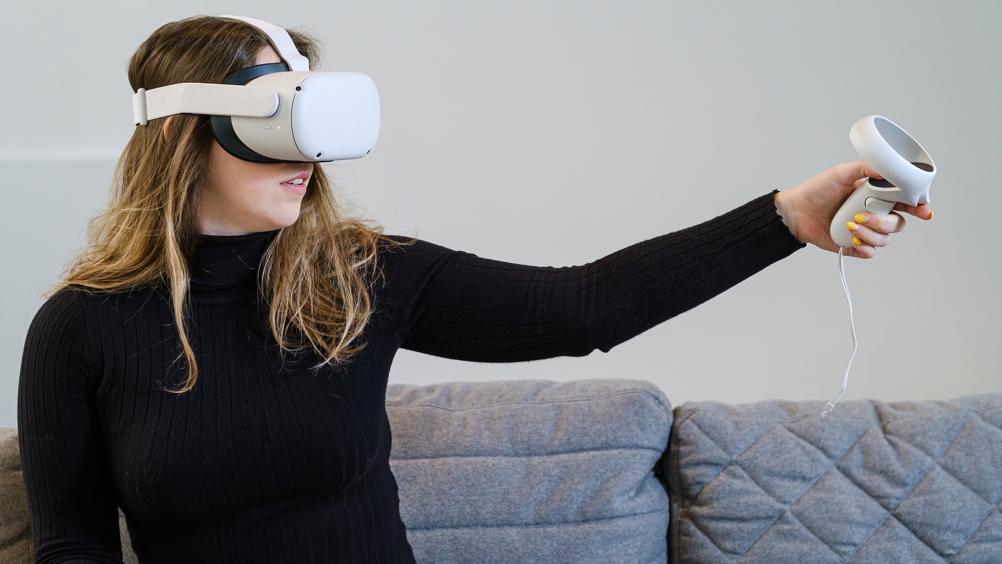 Junge Frau probiert die Oculus Quest 2 (Meta Quest 2) für ein virtuelles Erlebnis aus. Sie sitzt auf der Couch und trägt ein schwarzes Oberteil