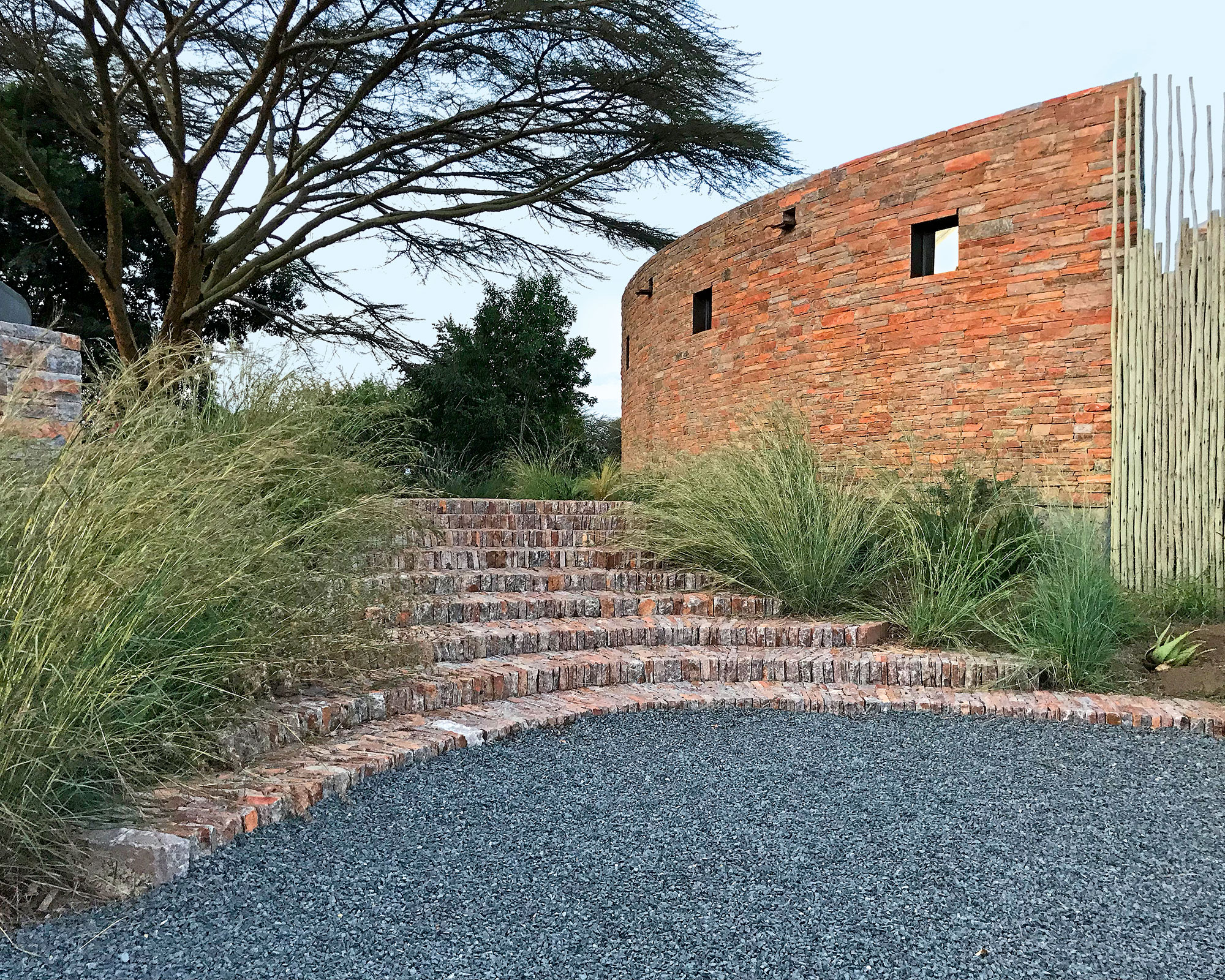 Brick steps and gray gravel, grass plants, curvaceous red brick wall