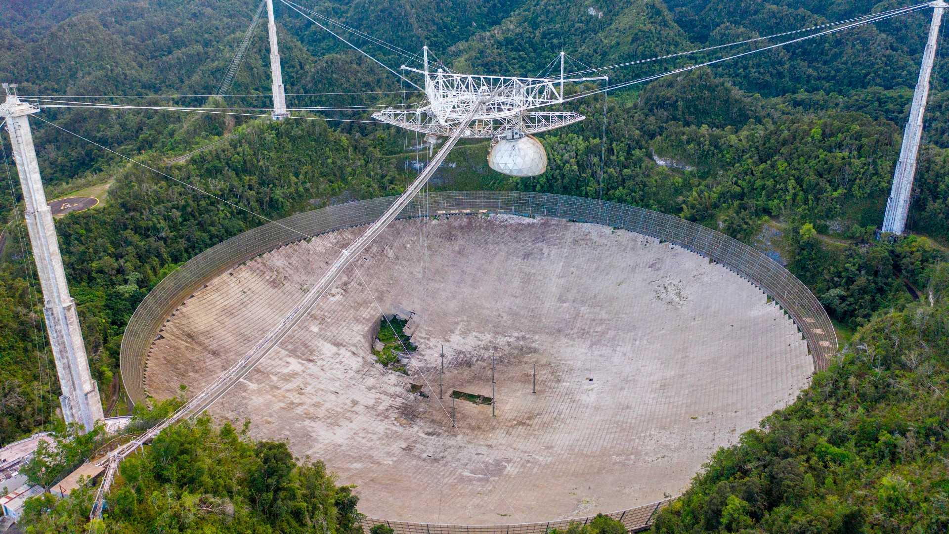 arecibo telescope aerial view showing equipment suspended via cable. damage is visible below