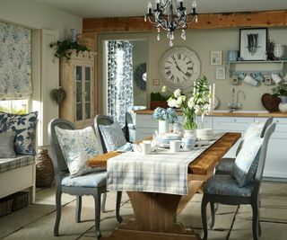 a country cottage with wooden dining table, blue and white soft furnishings and chandelier hanging above the table