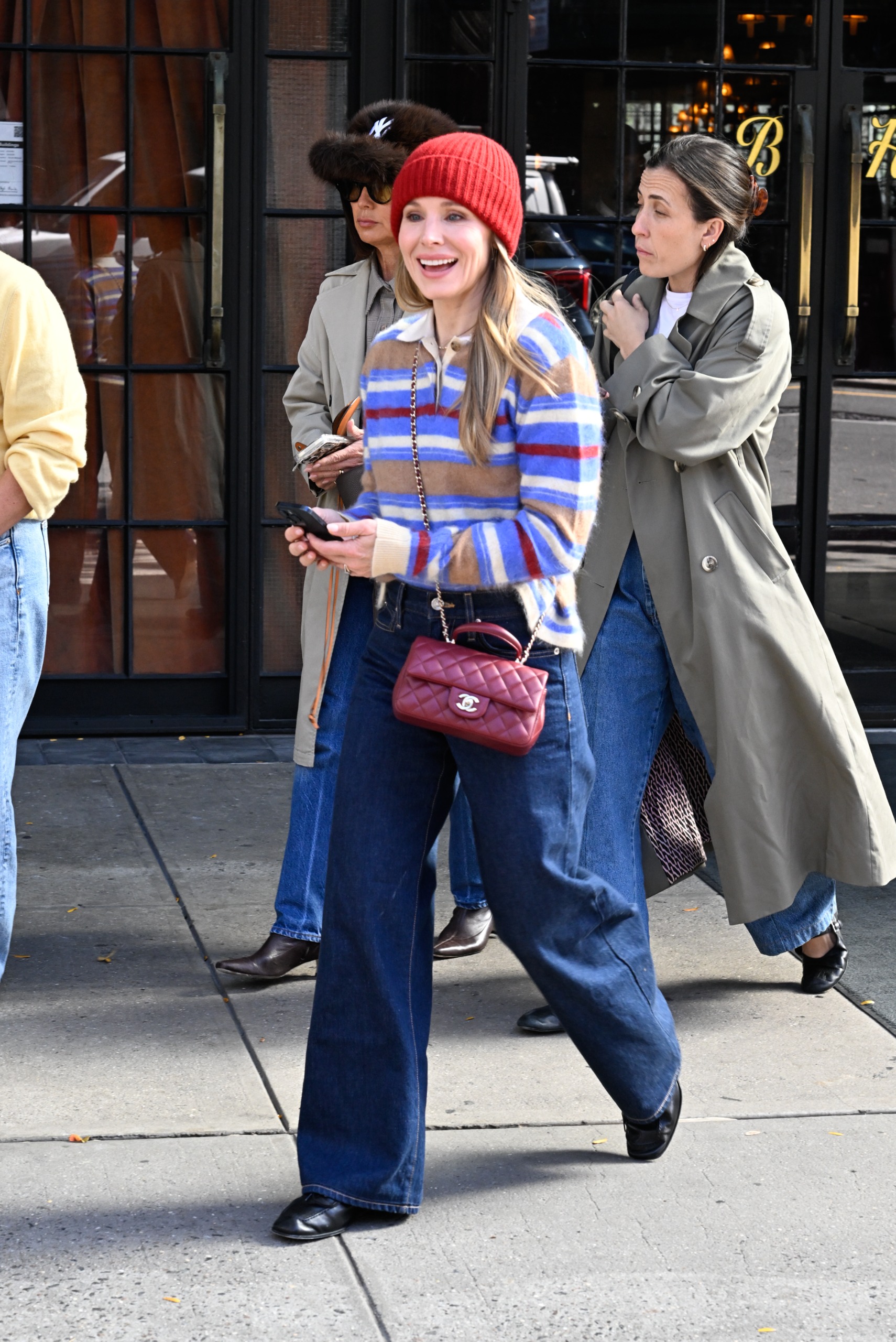 Kristen Bell walks outside wearing a striped polo jumper with indigo jeans, a burgundy Chanel bag and black slim-line leather trainers.