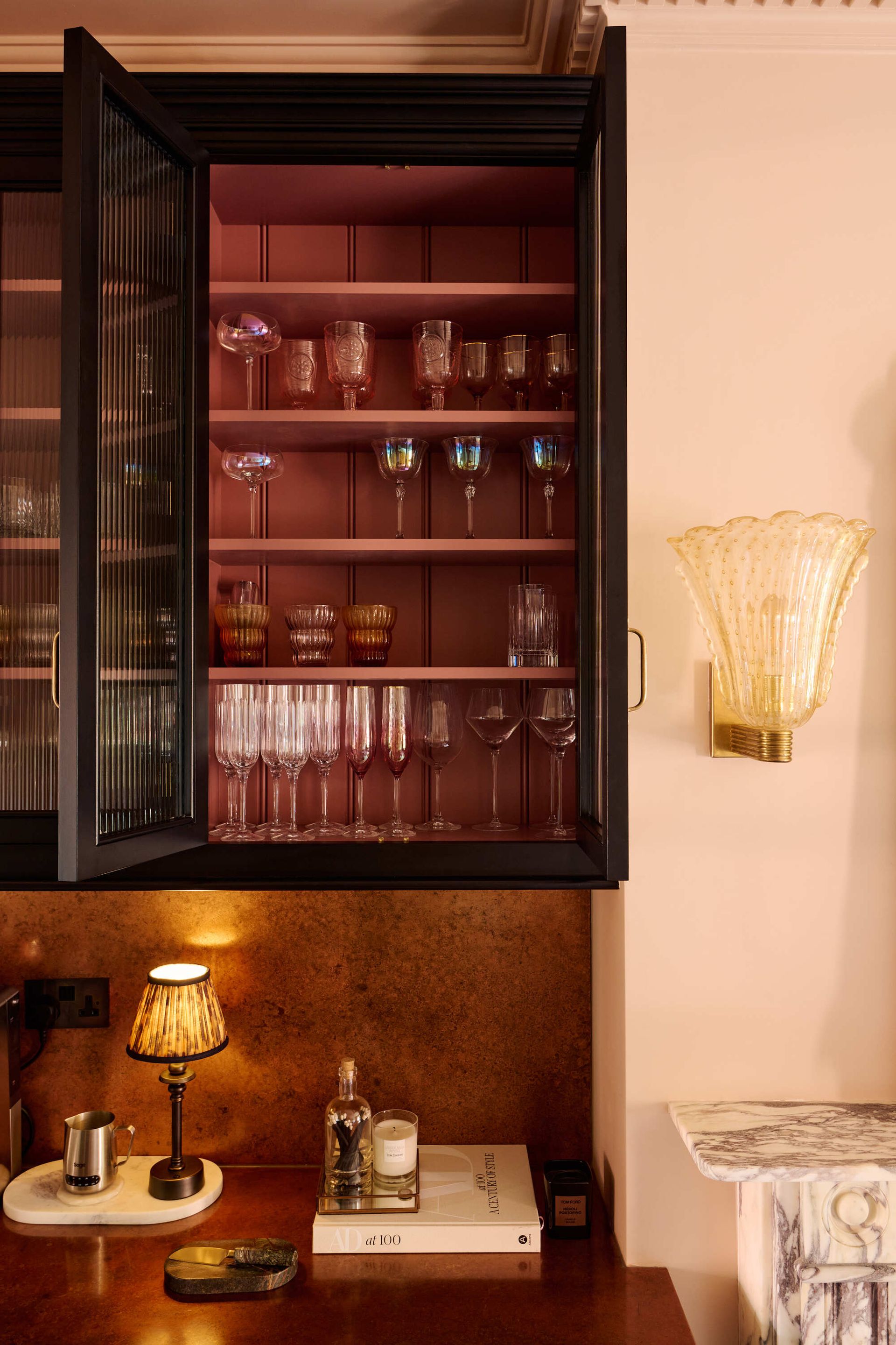 An open glass fronted kitchen cabinet with coloured glassware