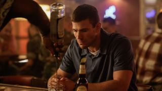 Austin Stowell's Gibbs sitting at a bar looking sad while a drink is poured for him