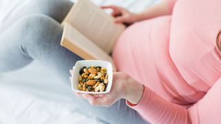 A woman sat in bed reading holding a bowl of assorted nuts