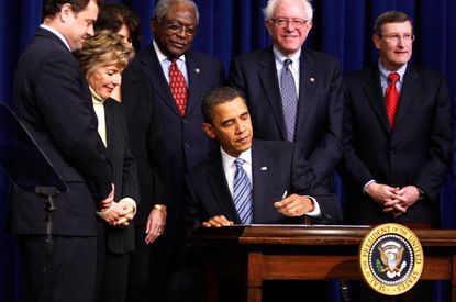 President Obama signs an act as senators, including Bernie Sanders, watch.