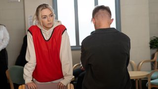 Lauren Bolton looks worried wearing a prison apron as Max Turner sits beside her with his back to the camera in Coronation Street.