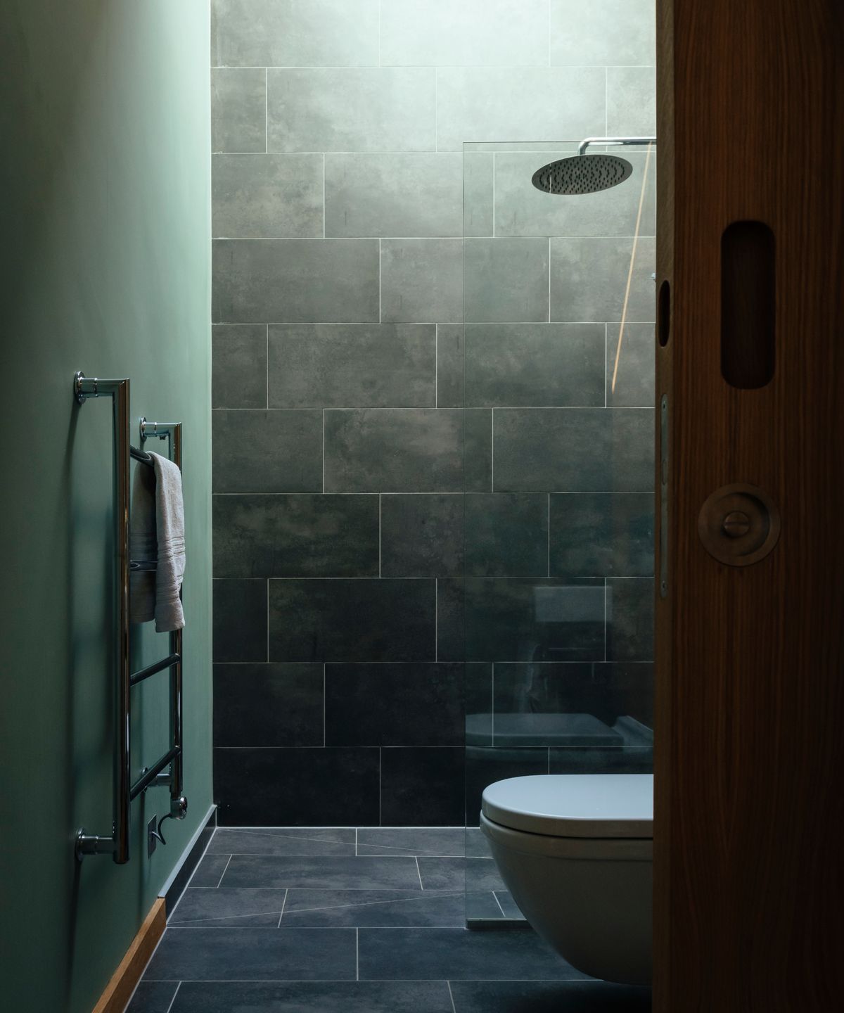 bathroom with wooden pocket sliding door, green painted wall, green tiled wall and grey tiled floor