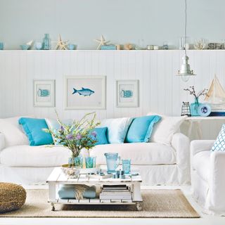 White linen sofa with blue cushions in front of white panelled wall in nautical themed room