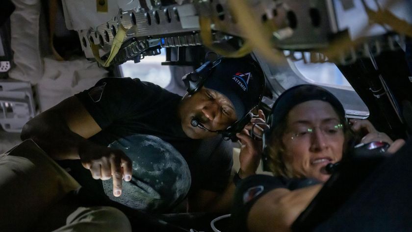 A man and a woman hunch over in a small capsule, both looking at separate electronic screens