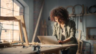 An artist using a laptop on a table in a studio that looks like a loft