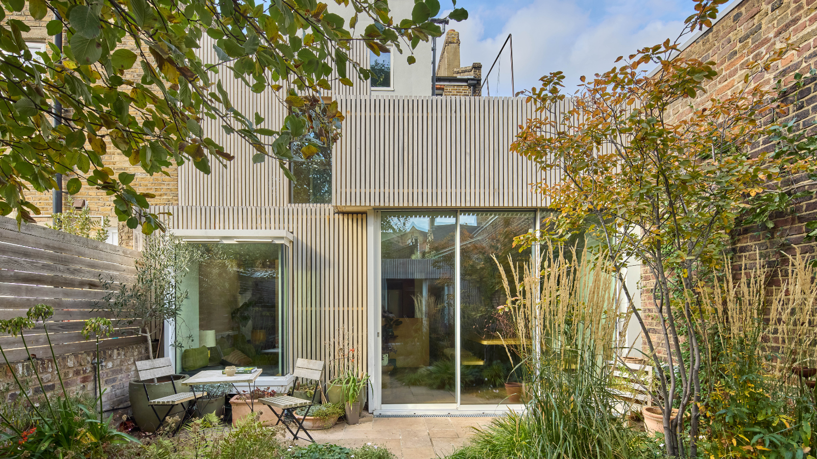 Exterior of a house with wooden cladding and a patio in front with a table and chairs