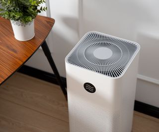 A white air purifer on the floor beside a side table and house plant