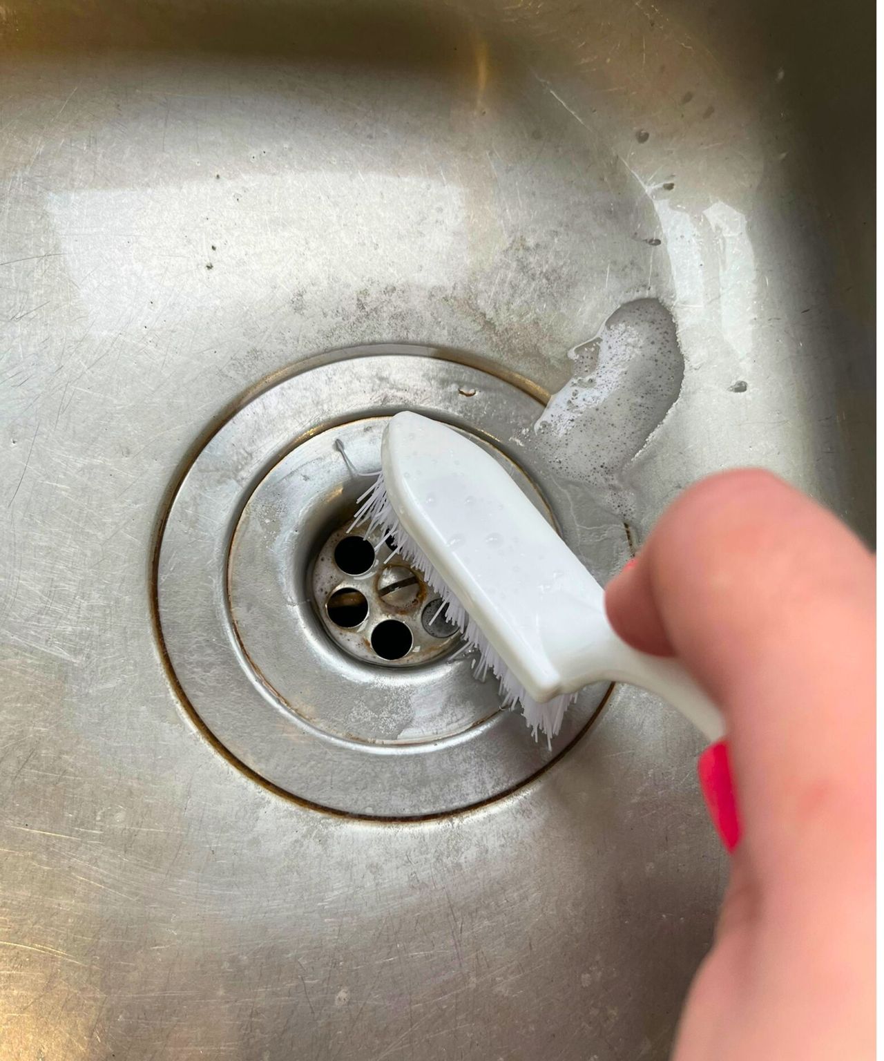 Close up of stainless steel sink drain with tea and coffee stains being cleaned by a scrubbing brush