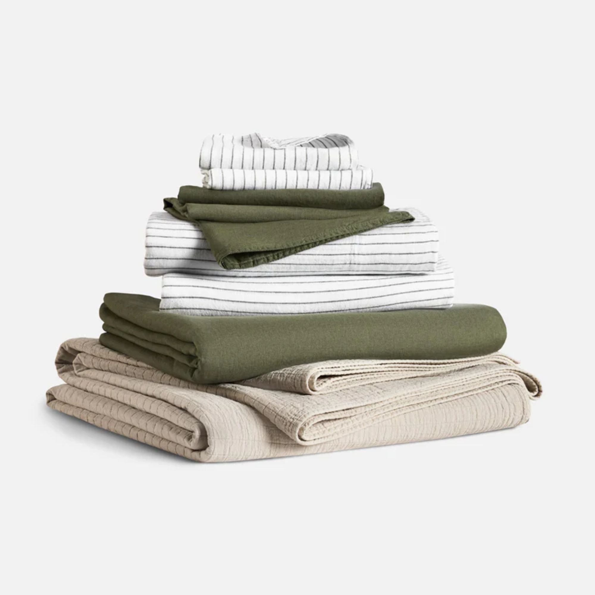 Folded set of white striped sheets with green linen pillowcases and a muslin quilt