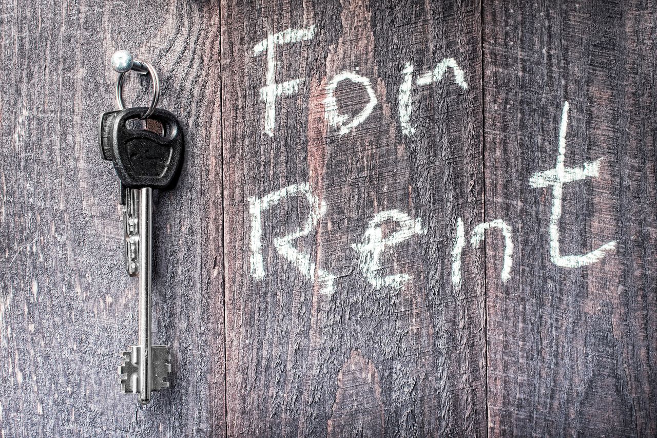 A bunch of keys hanging on a carnation on a wooden background, the inscription &quot;for Rent