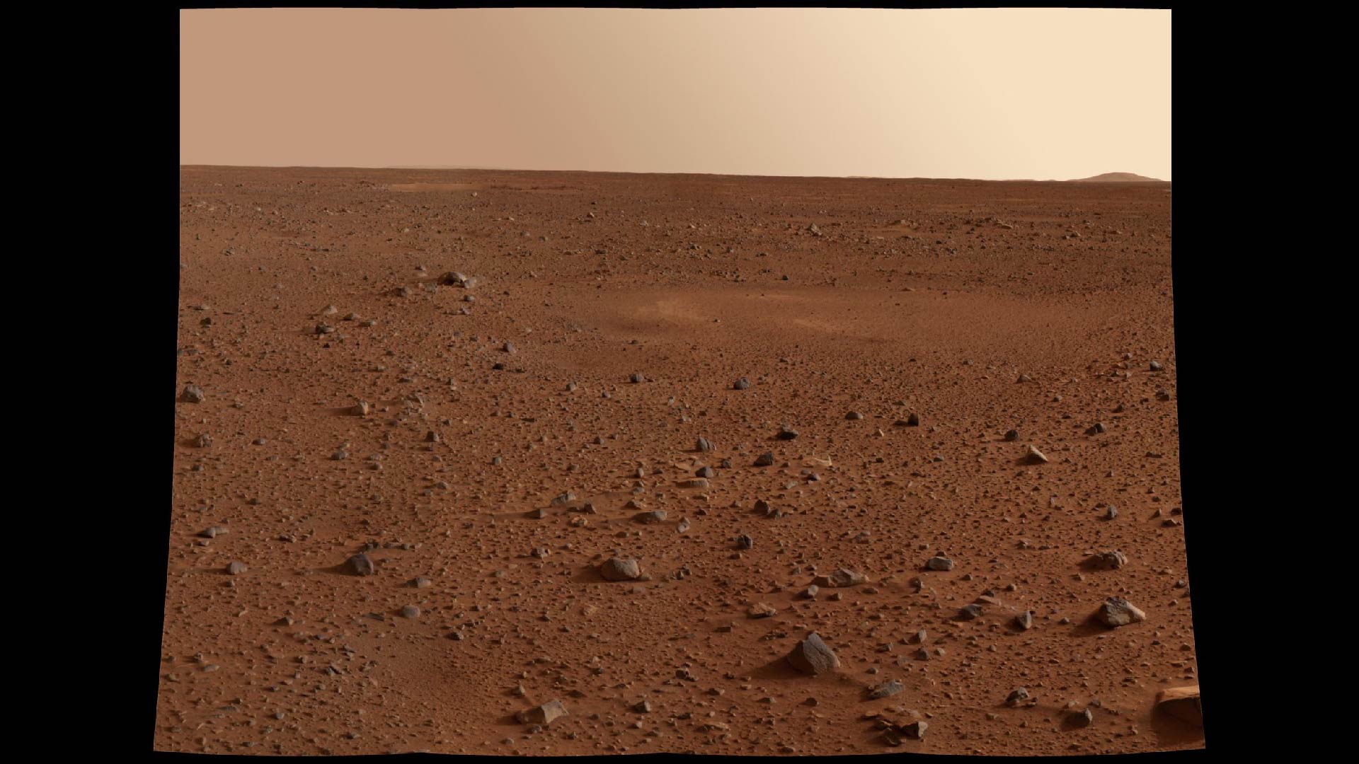 A photograph on the surface of Mars. It features red dirt and rocks in a barren landscape with a light yellow sky.