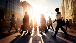 People walking across busy city street with sunrise in background.