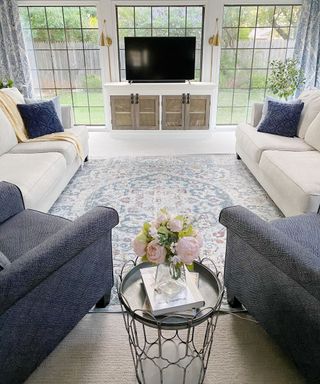 Living room with two blue arm chairs, cream couches and a blue patterned area rug