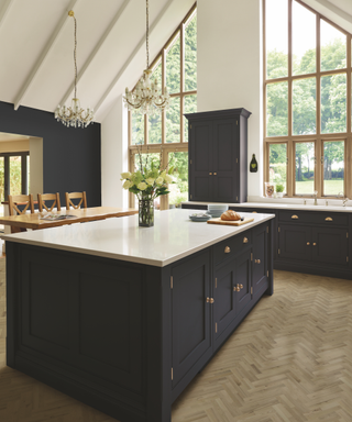 A dark blue kitchen with large windows and a chandelier kitchen lights design.