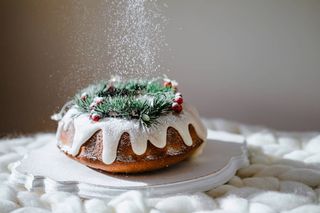 Gingerbread cake for Christmas with lingonberry and christmas decorations over wool white background. Homemade lemon bundt cake with glaze and icing sugar.