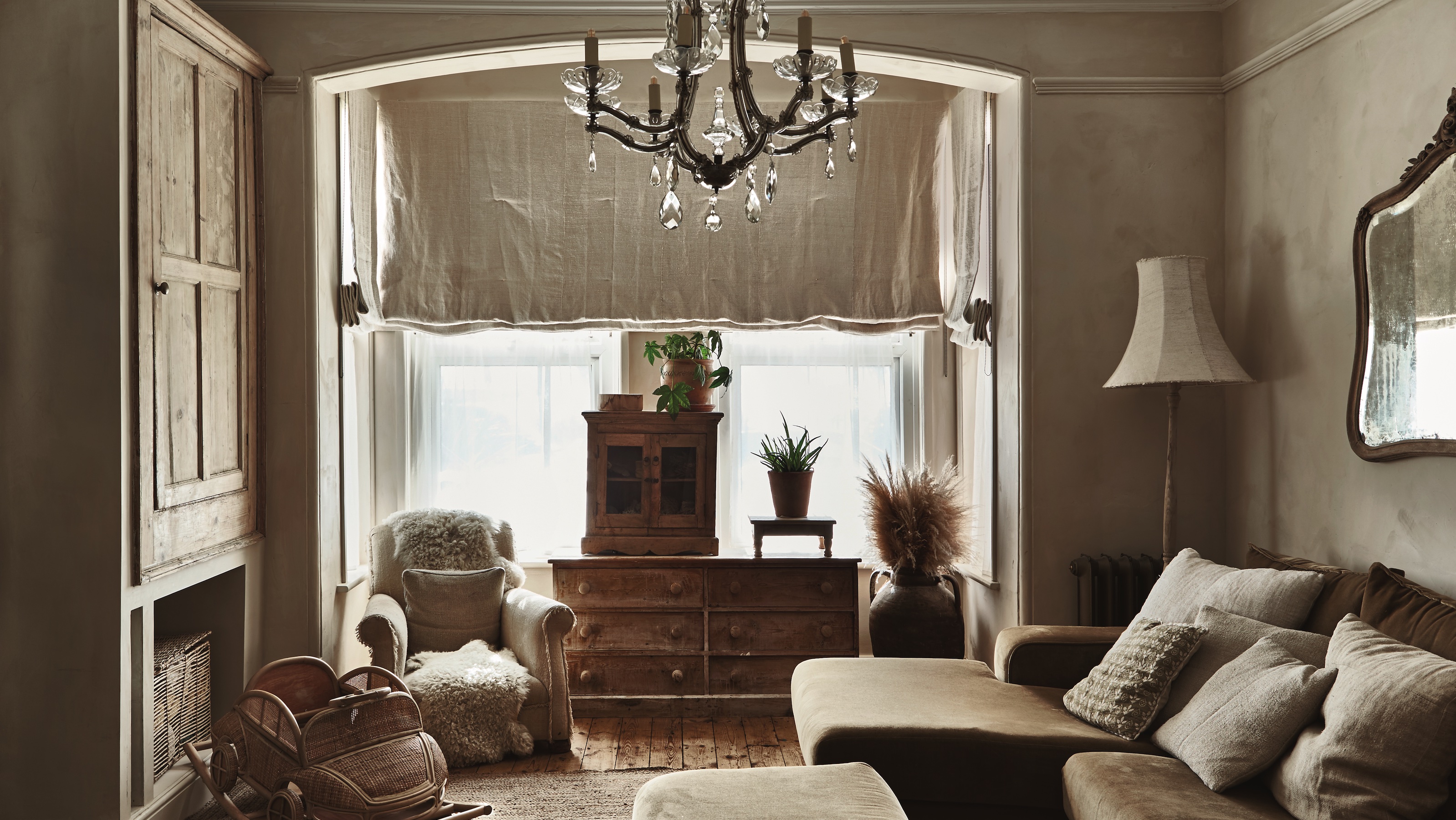 neutral sitting room with linen curtain, raw wood furniture, green velvet corner sofa and rush rug