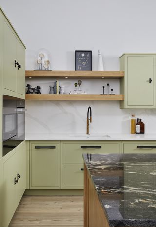 a sage green kitchen with a marble splashback and brass tap