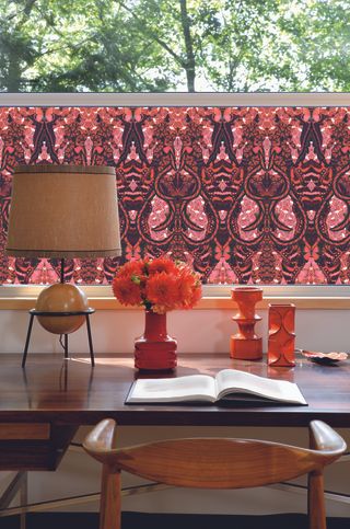 desk space with bright floral window film, a large lamp, and red decorative glass vases