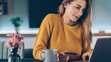 A smiling woman pays online with credit card using a laptop at home