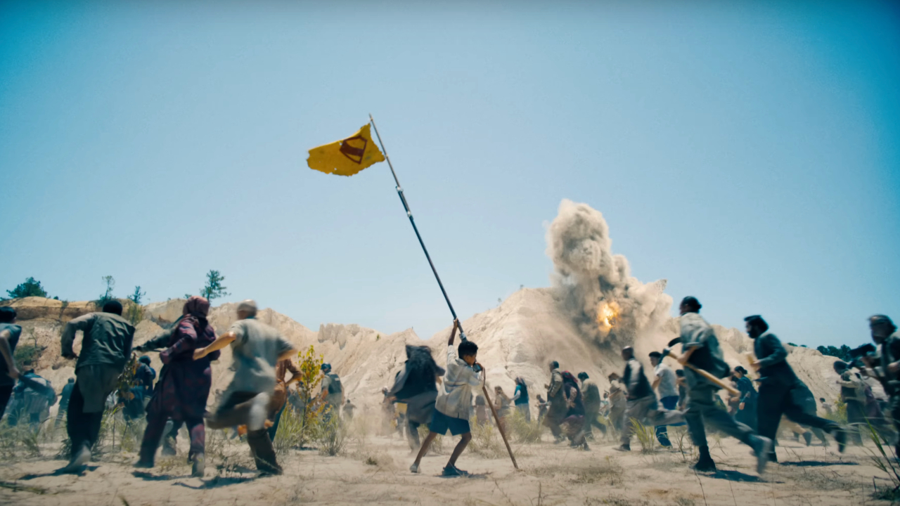 A child in Jarhanpur hoists a Superman flag as adults run from an explosion in Superman.