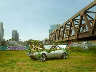 A car with flowers spilling out of it under a bridge in a grassy park