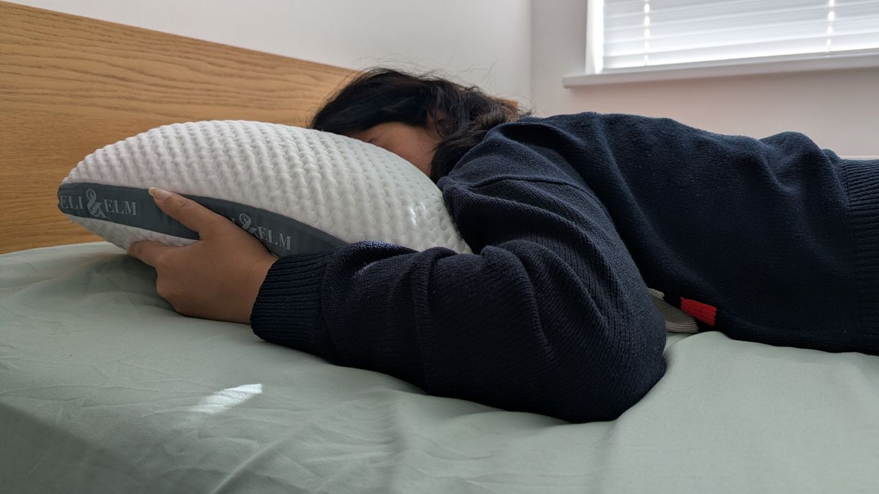 Woman sleeping on the Eli and Elm Side Sleeper Pillow in a bright lit room on the bed with a green bedsheet