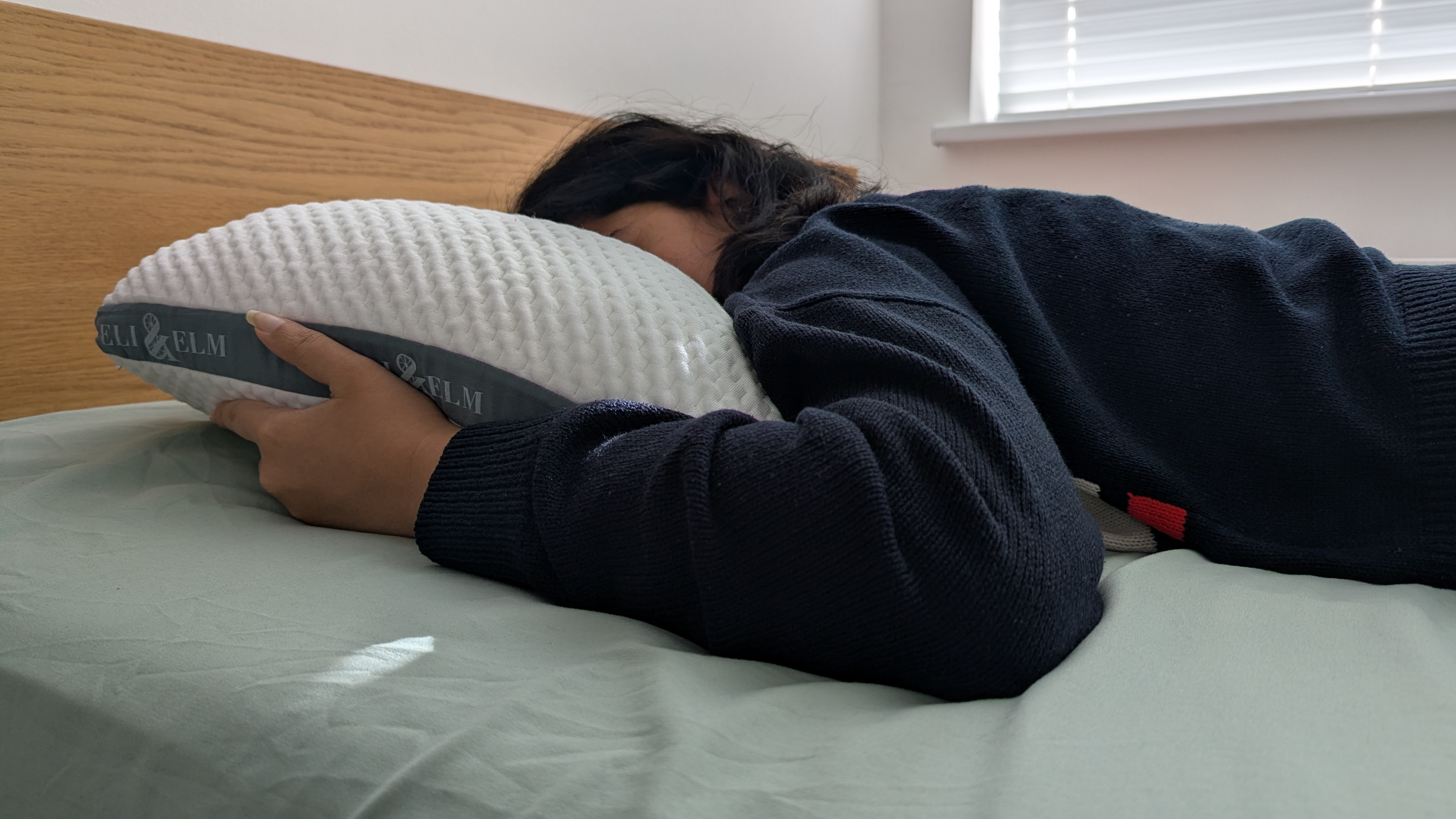 Woman sleeping on the Eli and Elm Side Sleeper Pillow in a bright lit room on the bed with a green bedsheet
