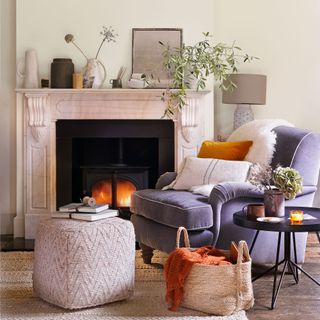 Off white living room with velvet grey armchair next to an open fire