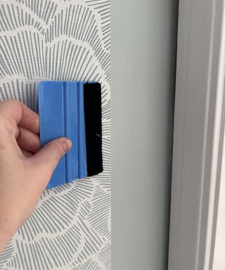 Dori Turner using smoothing tool on blue/grey peel and stick wallpaper decor