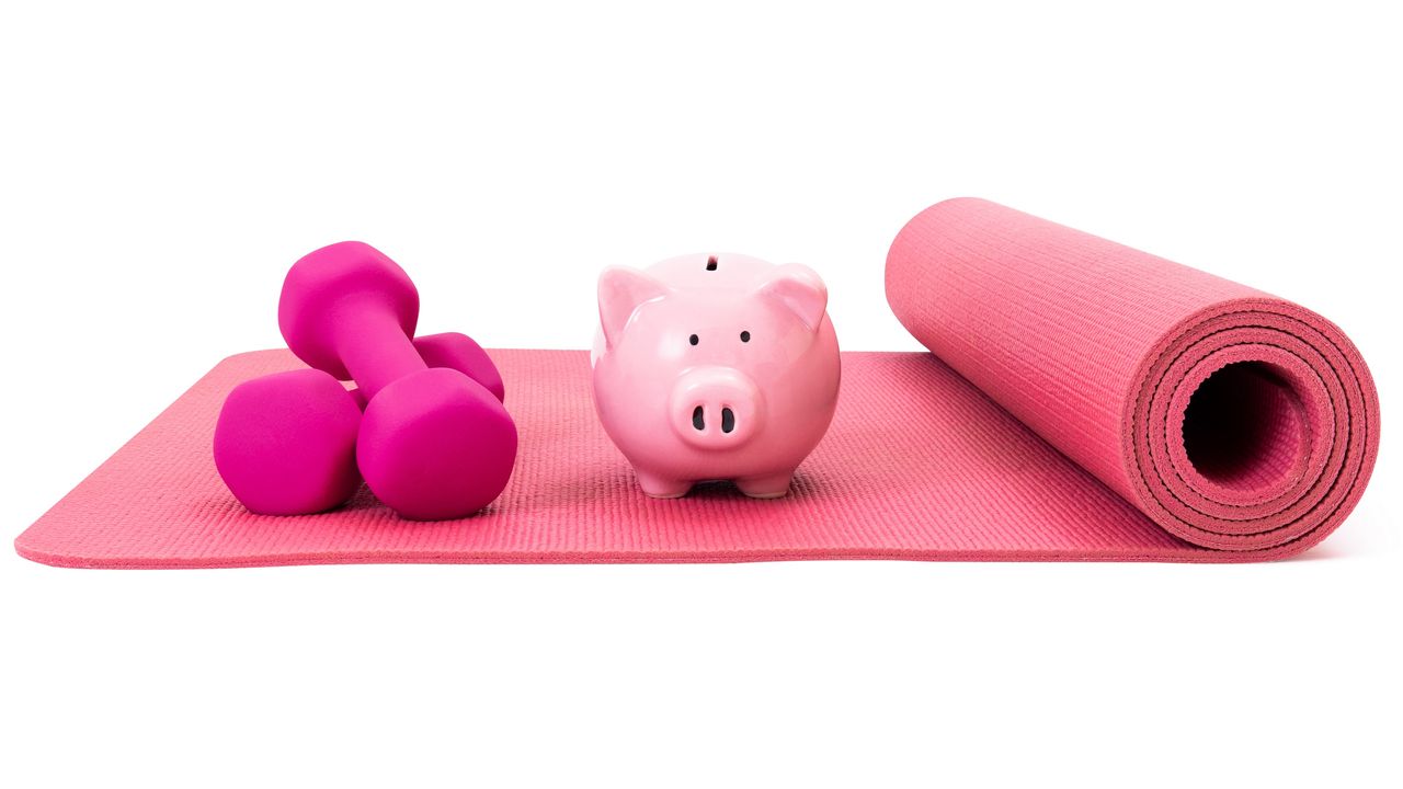 A piggy bank sits on a half-rolled yoga mat next to a pair of dumbbells. 