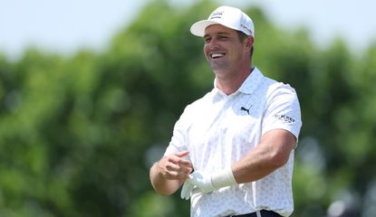 Bryson DeChambeau smiles whilst putting on his golf glove over a heavily taped wrist