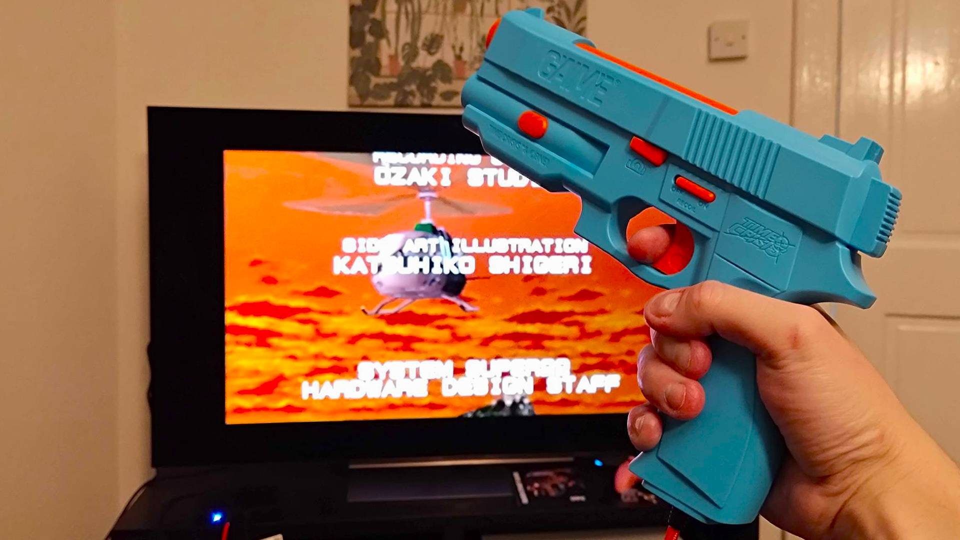 G&#039;AIM&#039;E Time Crisis console connected to TV with end credits rolling and hand holding gun.