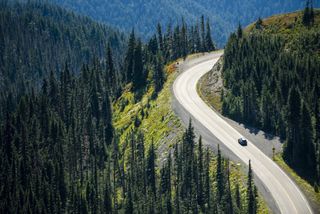 Forest of evergreens in the mountains with a singular road and a car driving on it