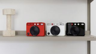Three variations of the Leica Sofort 2 camera on a shelf; in red, white and black