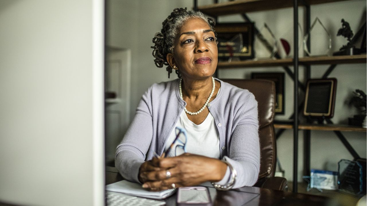 An older woman sits at her table and appears to be thinking about something serious.