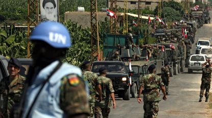 TOPSHOT - A convoy of Lebanese army military vehicles drive past a portrait of the late leader of Iran's Islamic revolution, Ayatollah Ruhollah Khomeini, at a UN checkpoint manned by Ghanaian peacekeeping forces in the coastal southern Lebanese city of Tyre, 08 September 2006. The UN Interim Force in Lebanon (UNIFIL) is tasked with enforcing a fragile truce between Israel and Hezbollah militants, and supporting the Lebanese army as it takes up positions in southern Lebanon.
