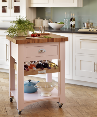 An example of portable kitchen island ideas showing a small pink portable kitchen island with a built in wine rack