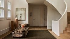 Entryway with spiral staircase, large olive green rug on wooden floor, tiger print daybed with velvet pink cushion and modern abstract painting in the background