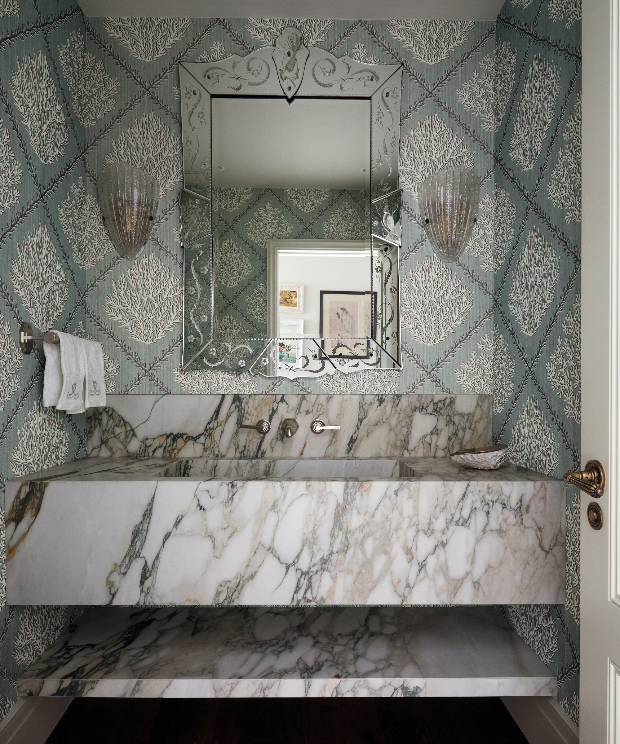 grand bathroom with large marble sink and seaweed wallpaper and bevelled mirror and glass wall lights