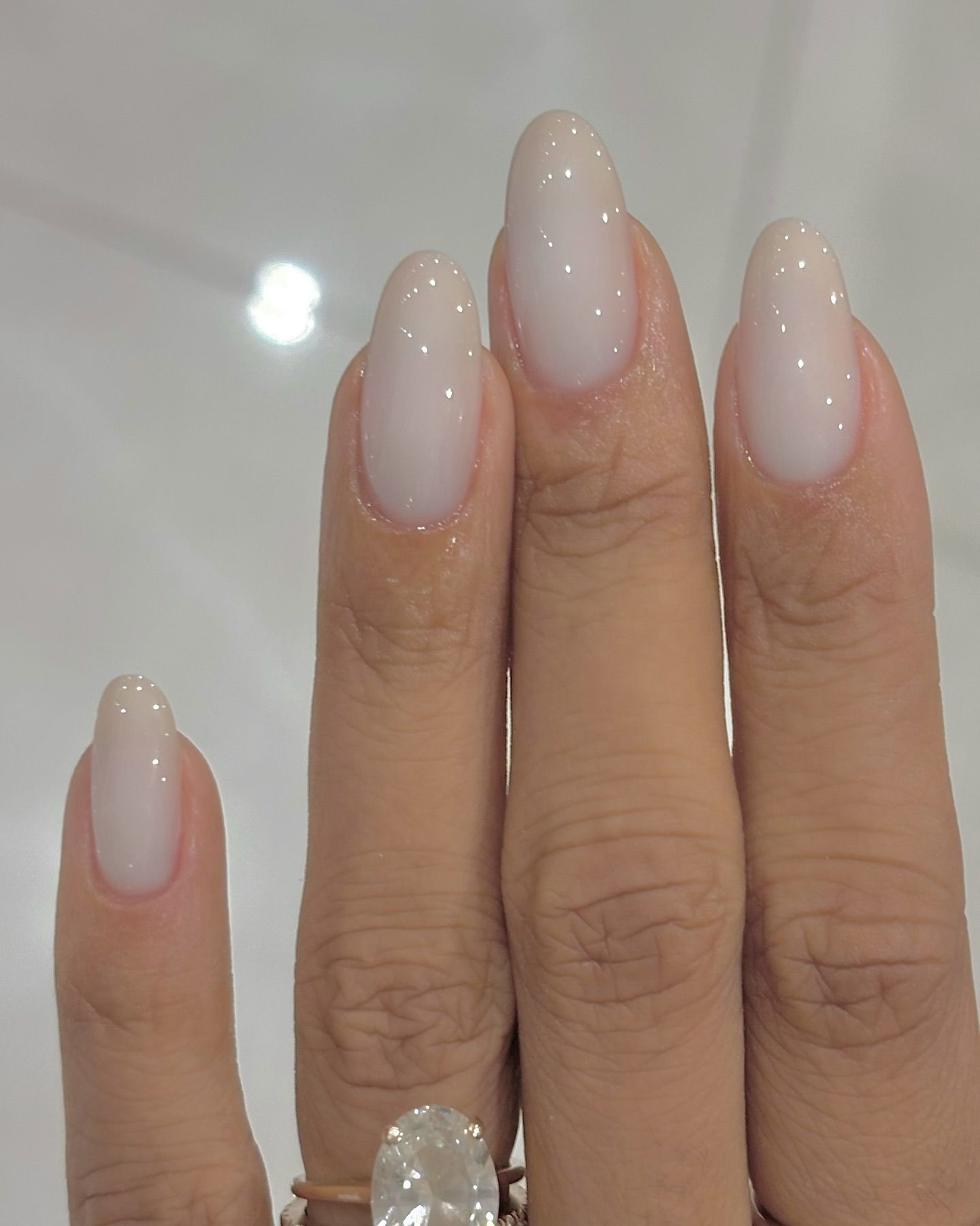 A close up of a milky manicure with sheer white nail polish on long almond nails