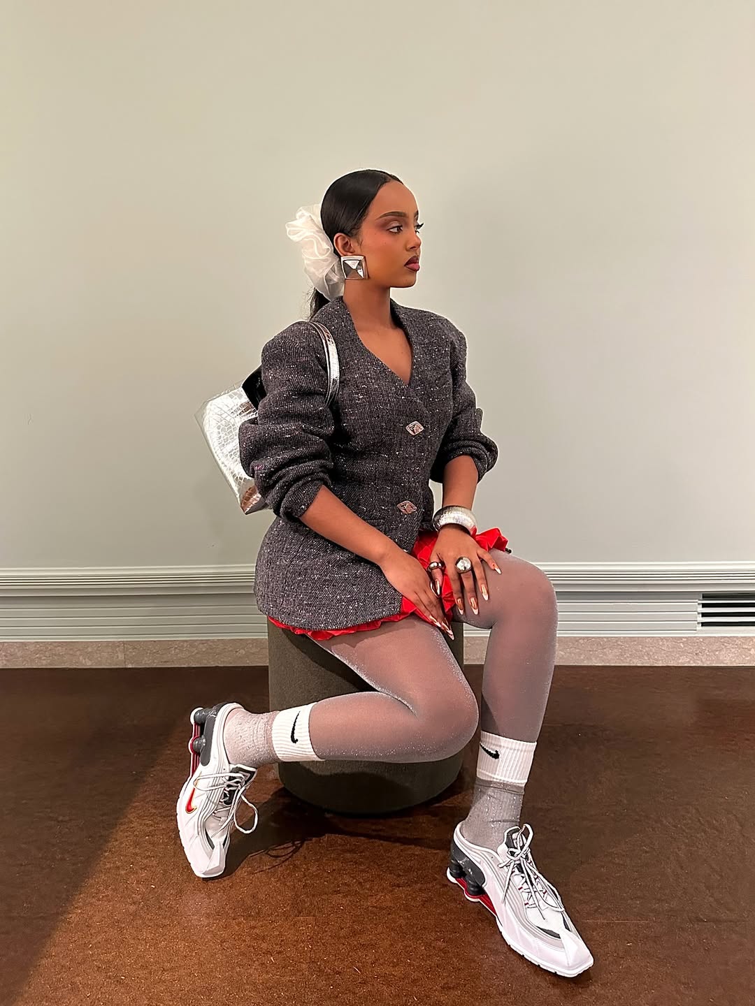 Black lily wears the Nike x Martine Rose Shox MR4 mules in white, grey and red with a grey jacket, red mini skirt and silver jewellery.