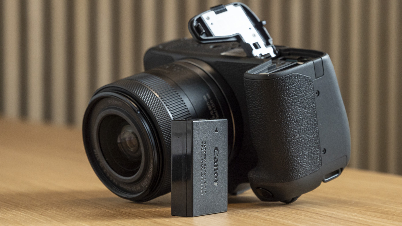 Canon EOS R8 upside down on a table with the battery door open and the battery on the table