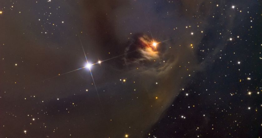 two bright stars, one white and one red, seen ins pace in a cloud of dust. many other smaller, fainter stars can be seen in the background